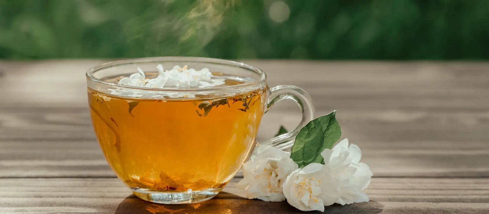 Tasse d'infusion au jasmin, fumante, sur une table en bois dans un jardin